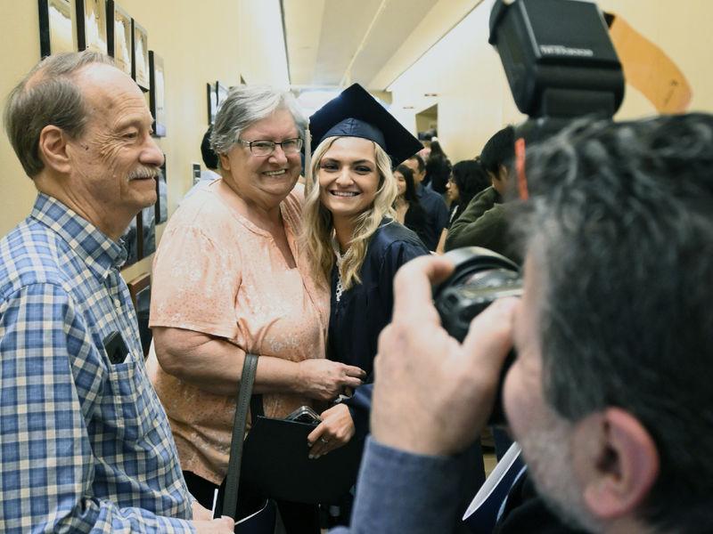 毕业生汉娜·摩根，戴着学士帽，穿着学士服，停下来和她的祖父母合影.