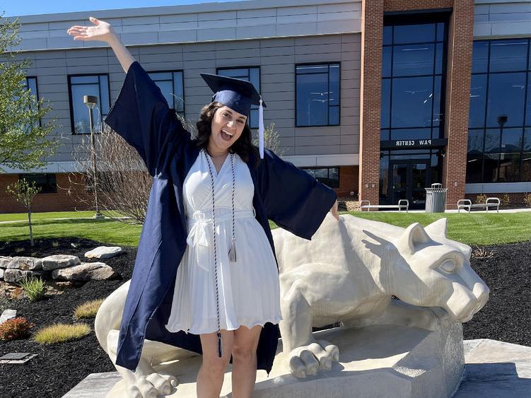 宾州州立大学新毕业生安娜·拉芬纳在宾州州立大学杜波依斯校区的狮子神殿前快乐地庆祝, 就在PAW中心外面